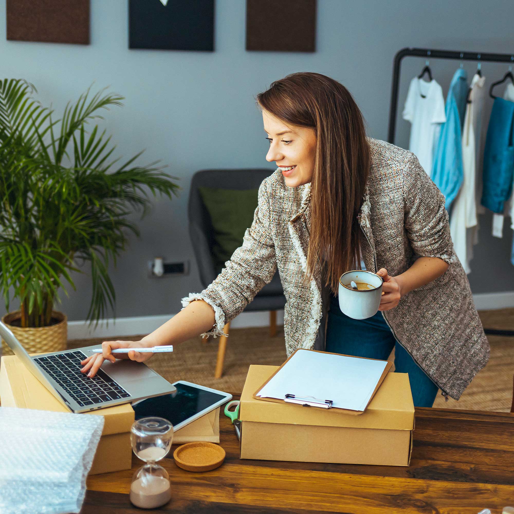 A woman holds a cup of coffee in one hand and types on a computer with the other.